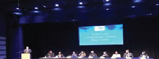 A panel seated at tables on stage with a projected title slide