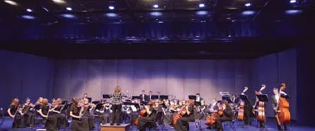 A student orchestra performing under blue stage light